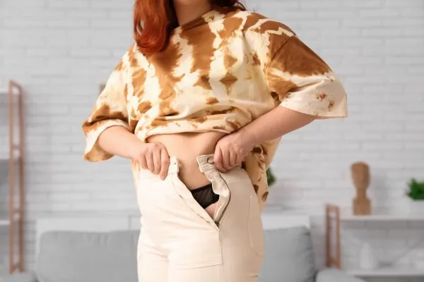 Image of woman trying to do her trousers up after pregnancy weight gain Witley
