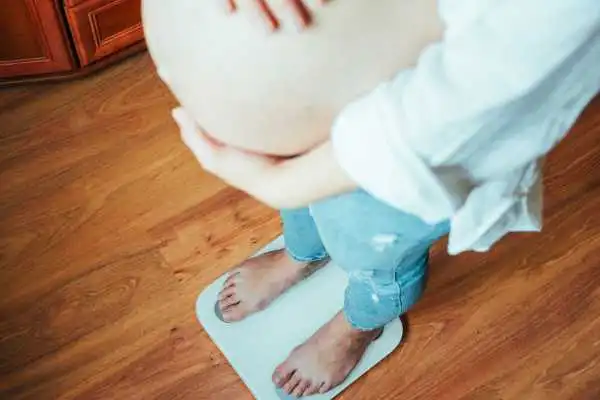 Image of woman weighing herself and experiencing weight gain through pregnancy Witley